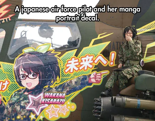 A smiling Japanese Air Force helicopter pilot in camouflage uniform sitting next to her helicopter, which features a large, colorful manga-style portrait decal of a female character also in camouflage.