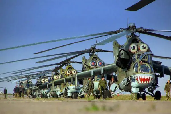 talk about angry birds A line of military helicopters on an airfield, each with humorous and exaggerated googly eyes painted on their cockpits and shark teeth painted on their noses, resembling the "Angry Birds" characters.