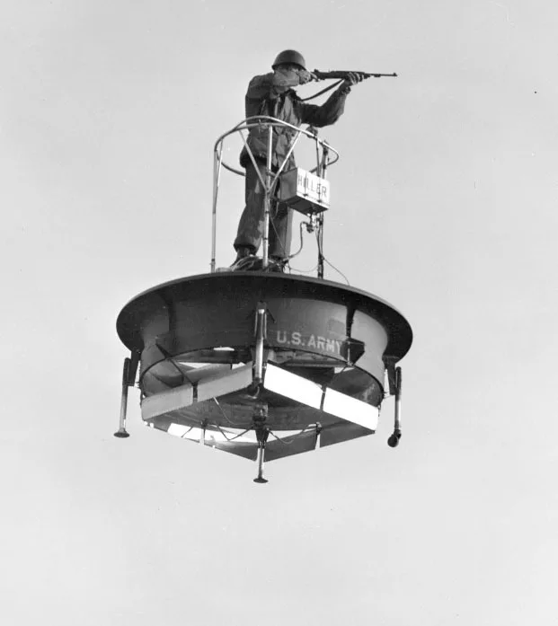 A black and white photo of a soldier standing on the Hiller VZ-1 Pawnee, an experimental personal flying platform, hovering in the air, representing a crazy aircraft concept that proved too impractical for operational use.